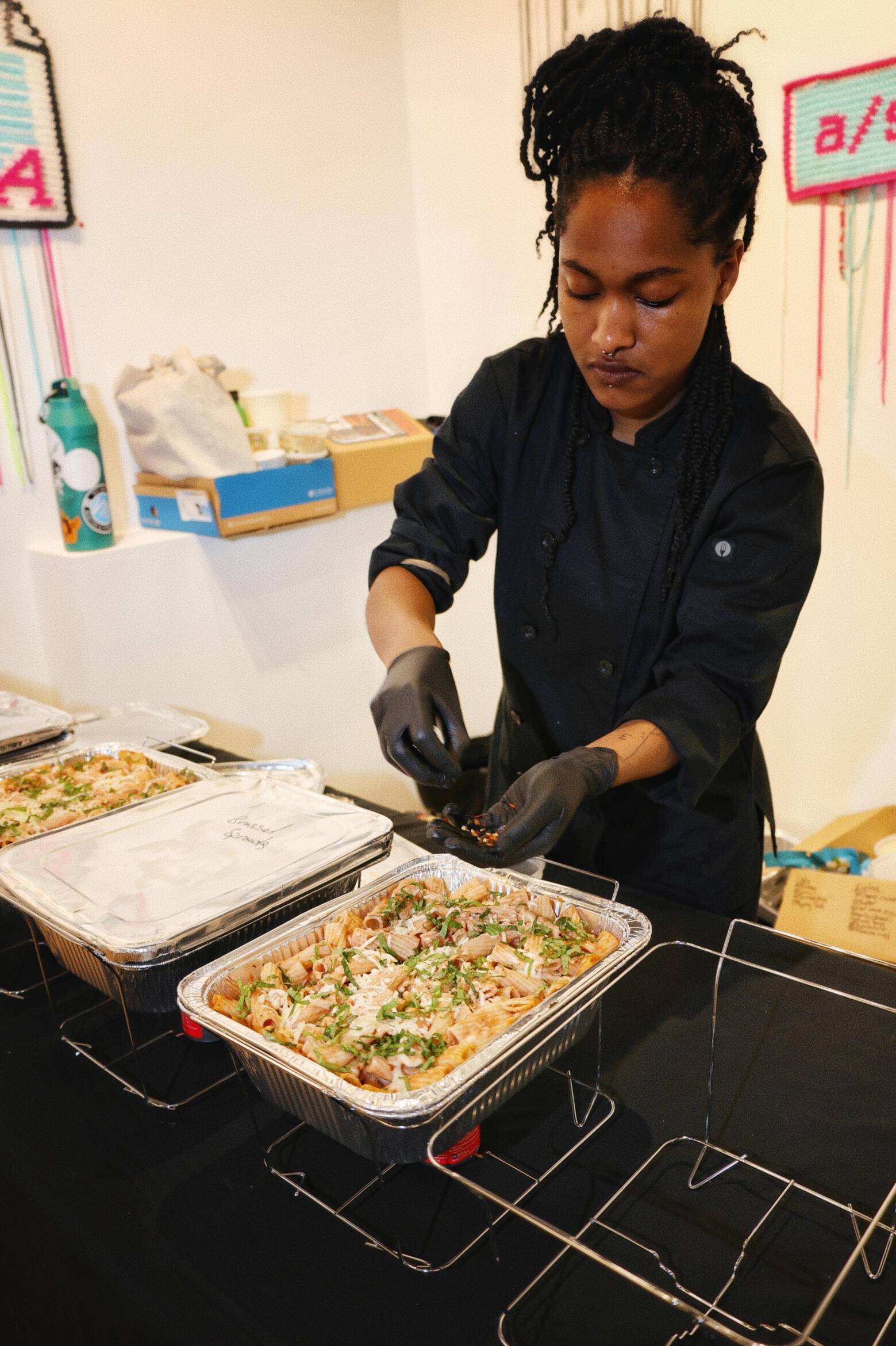 Orisa in a black chef coat plating from catering trays at an event