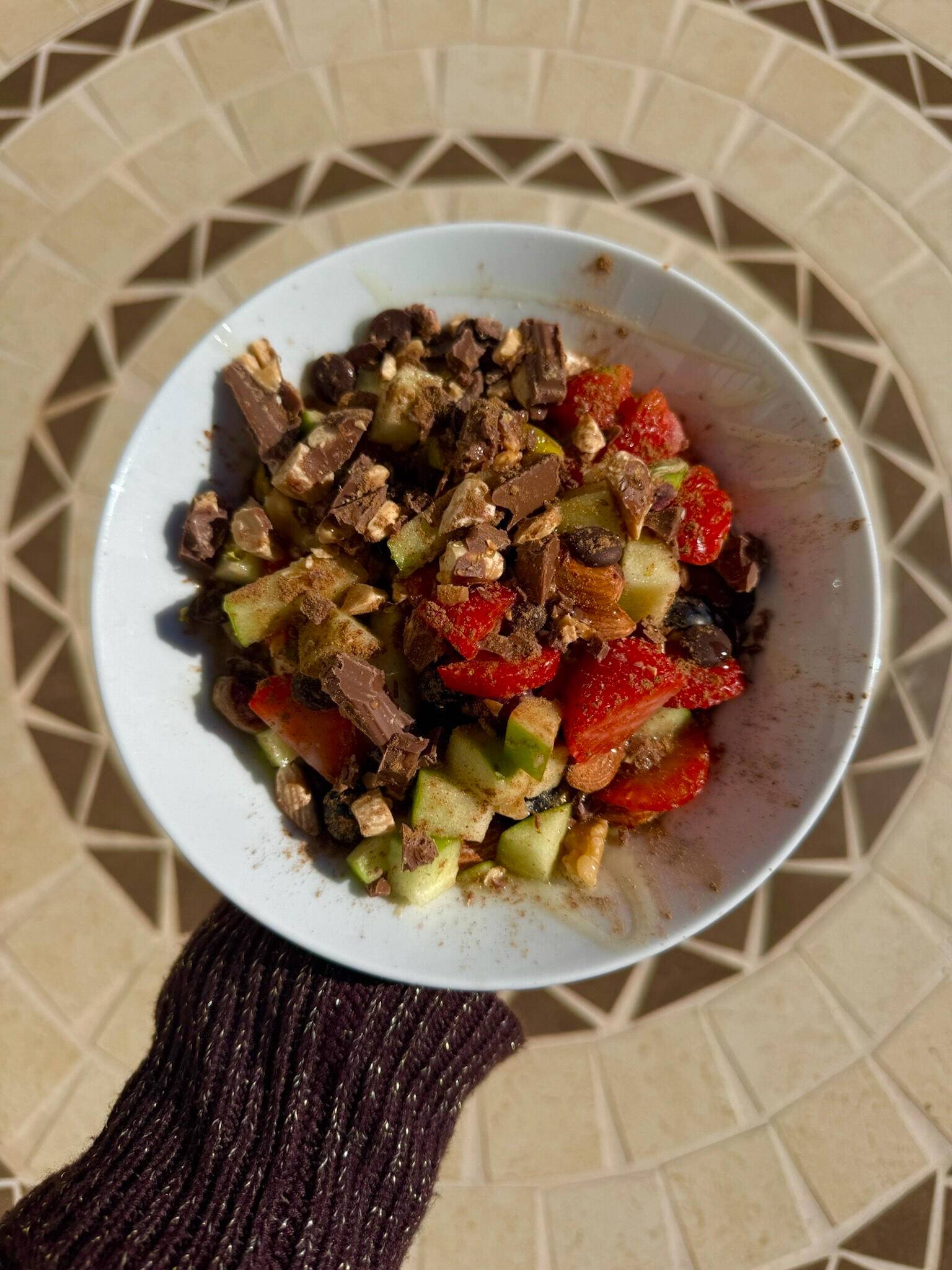 A white bowl of chopped chocolate, strawberries and cucumber on a mosaic table