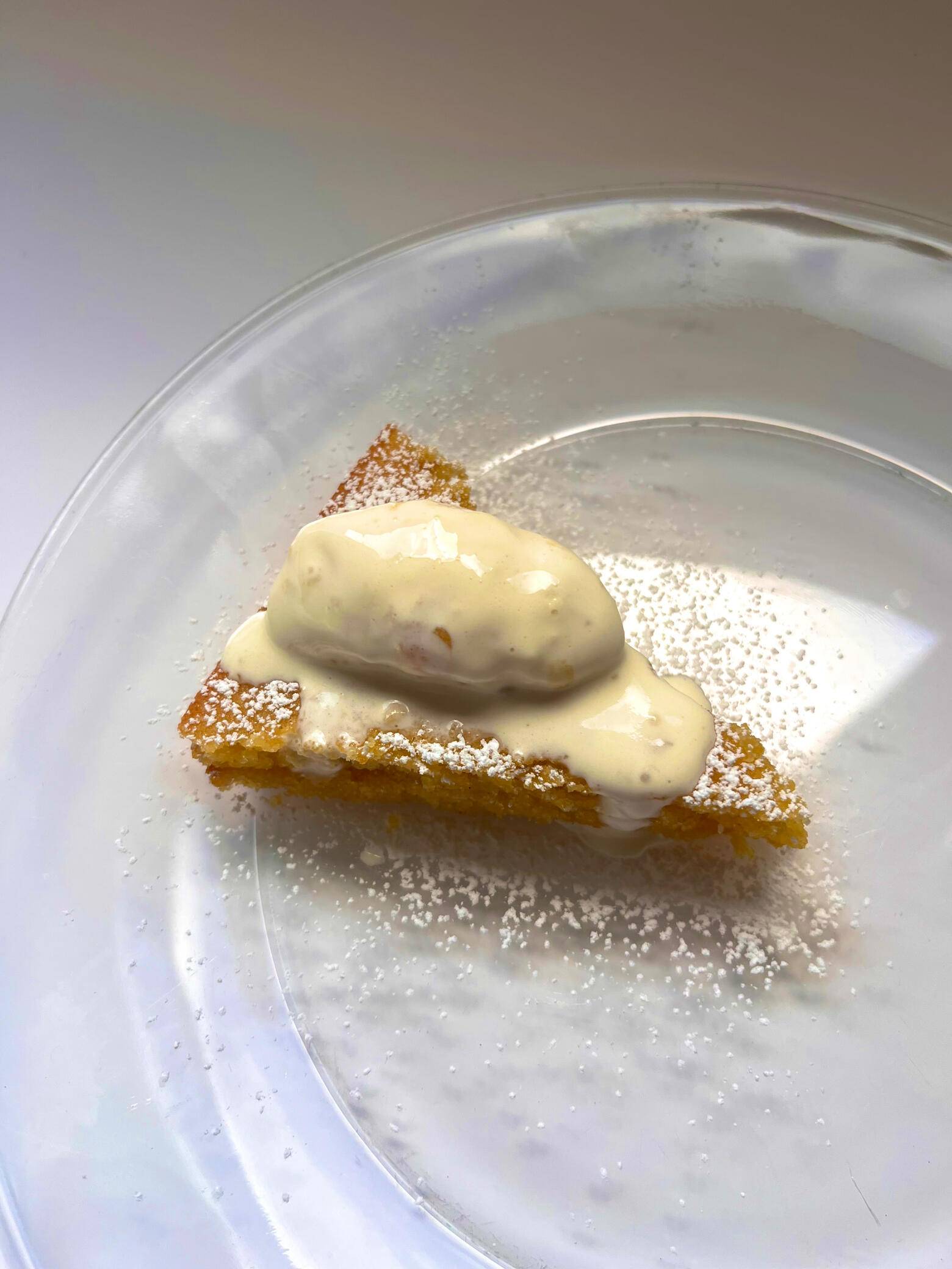 A dessert slice topped with cream and powdered sugar on a glass plate