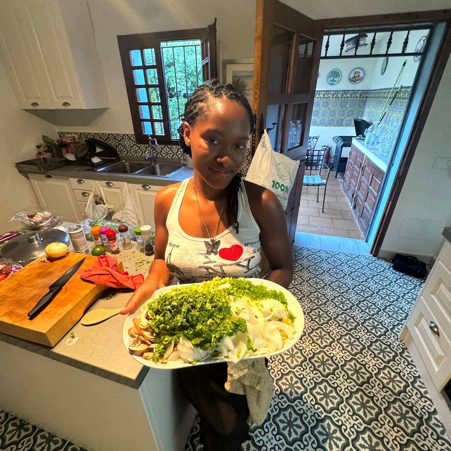Orisa in her kitchen, smiling and holding a platter of fresh greens