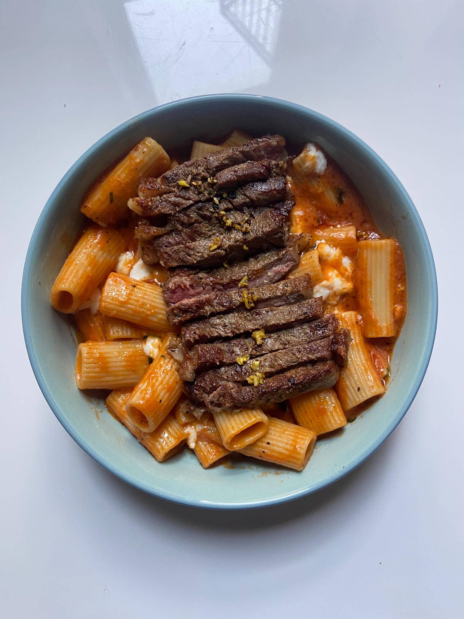 Rigatoni in a tomato cream sauce topped with sliced steak in a blue bowl