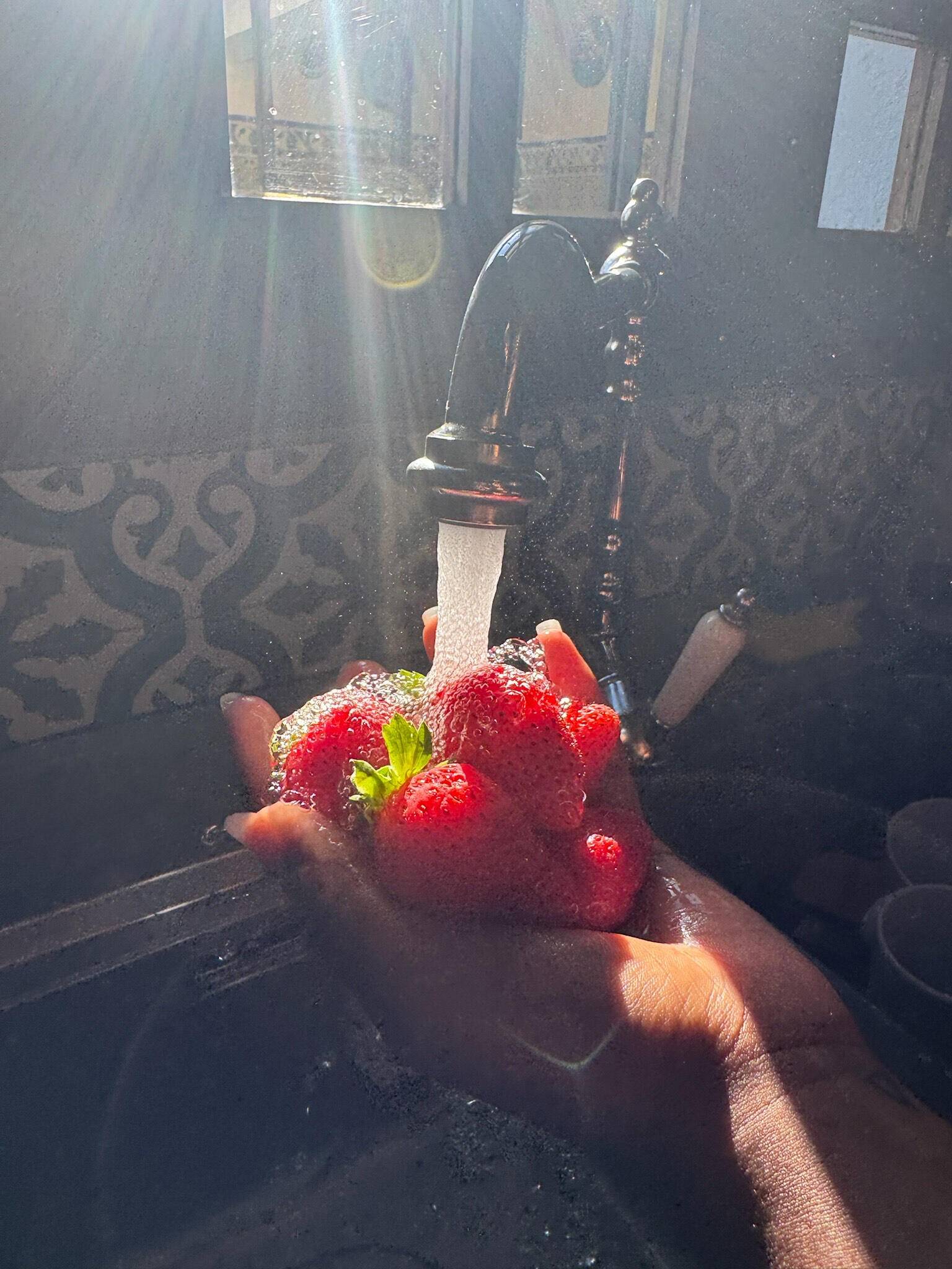 A handful of fresh strawberries rinsed under the tap in a beam of sunlight