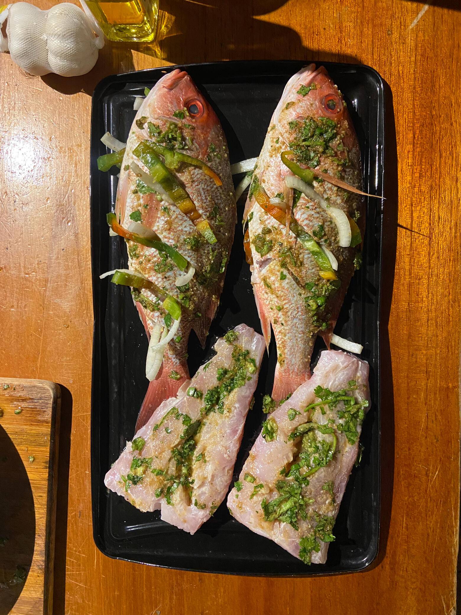 Whole fish and fillets scored and dressed with fresh herbs on a black tray